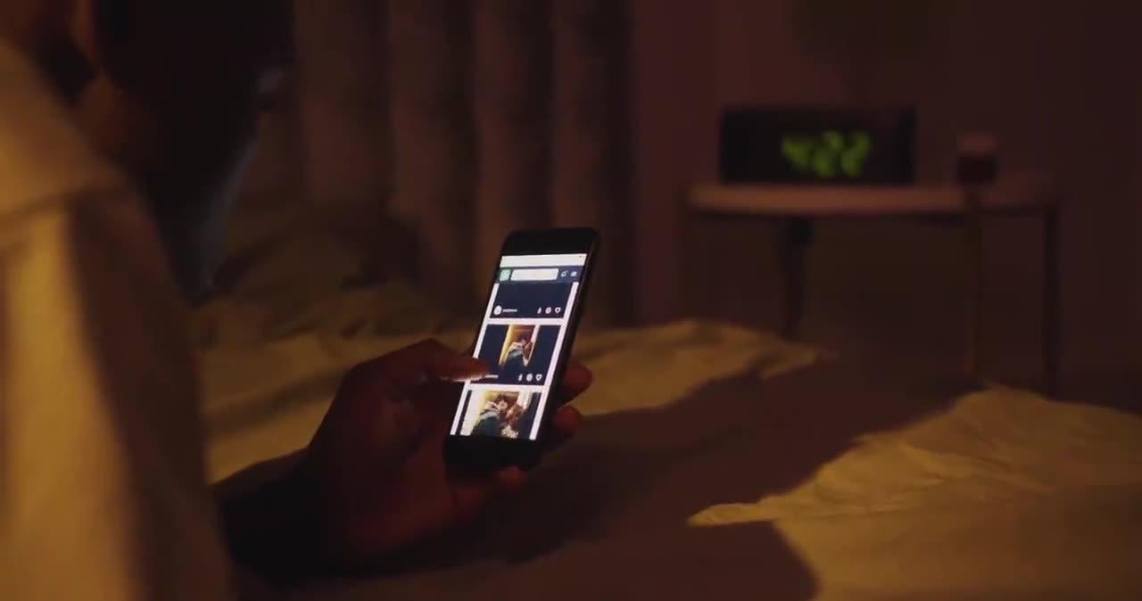 A dim bedroom at night, lit only by the screen of a phone held in two hands.